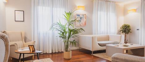 Un salon moderne avec un canapé, un fauteuil et une table basse. On y trouve une plante en pot et un tableau accroché au mur.