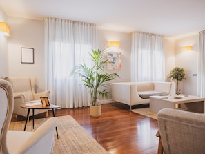 A modern living room with a sofa, armchair, and a coffee table. There is a potted plant and a painting on the wall.