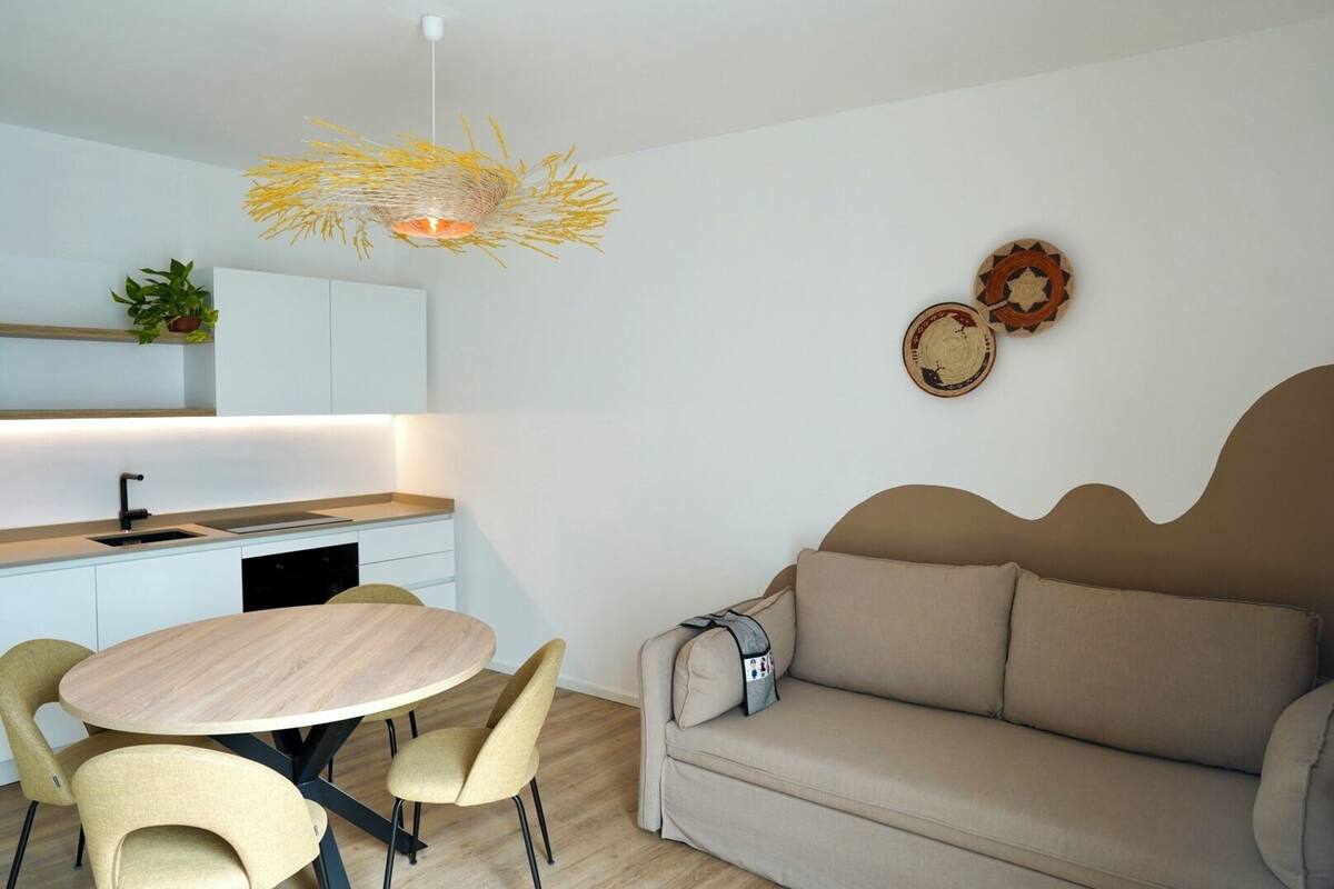 A modern living room with a round wooden table and chairs, a beige sofa, and a unique ceiling light fixture.