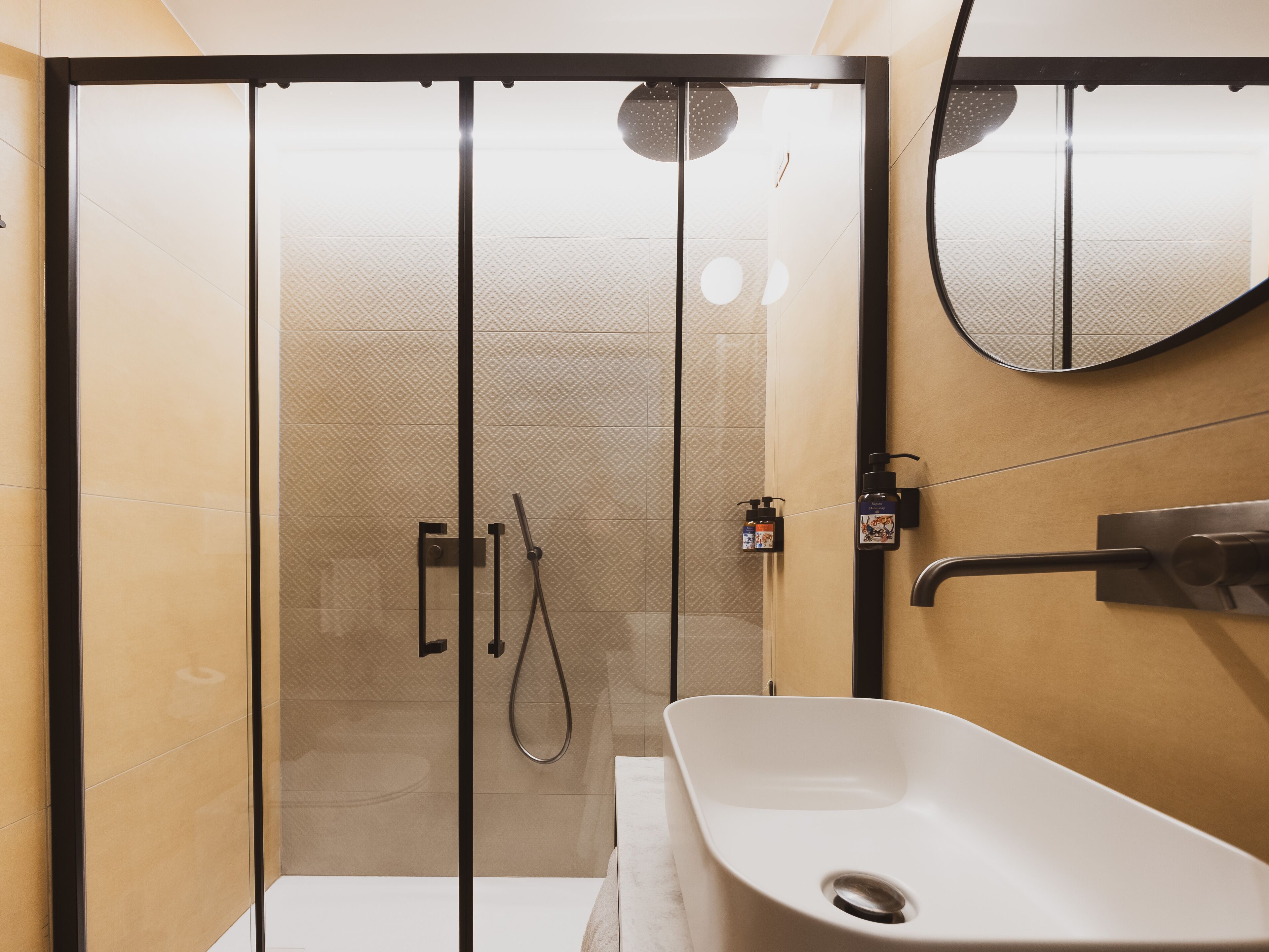 A modern bathroom with a glass-enclosed shower, a white bathtub, and a wall-mounted mirror.