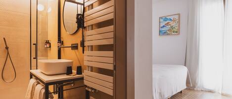 A modern bathroom with a glass-enclosed shower, a sink with a mirror, and a bedside table with a towel.