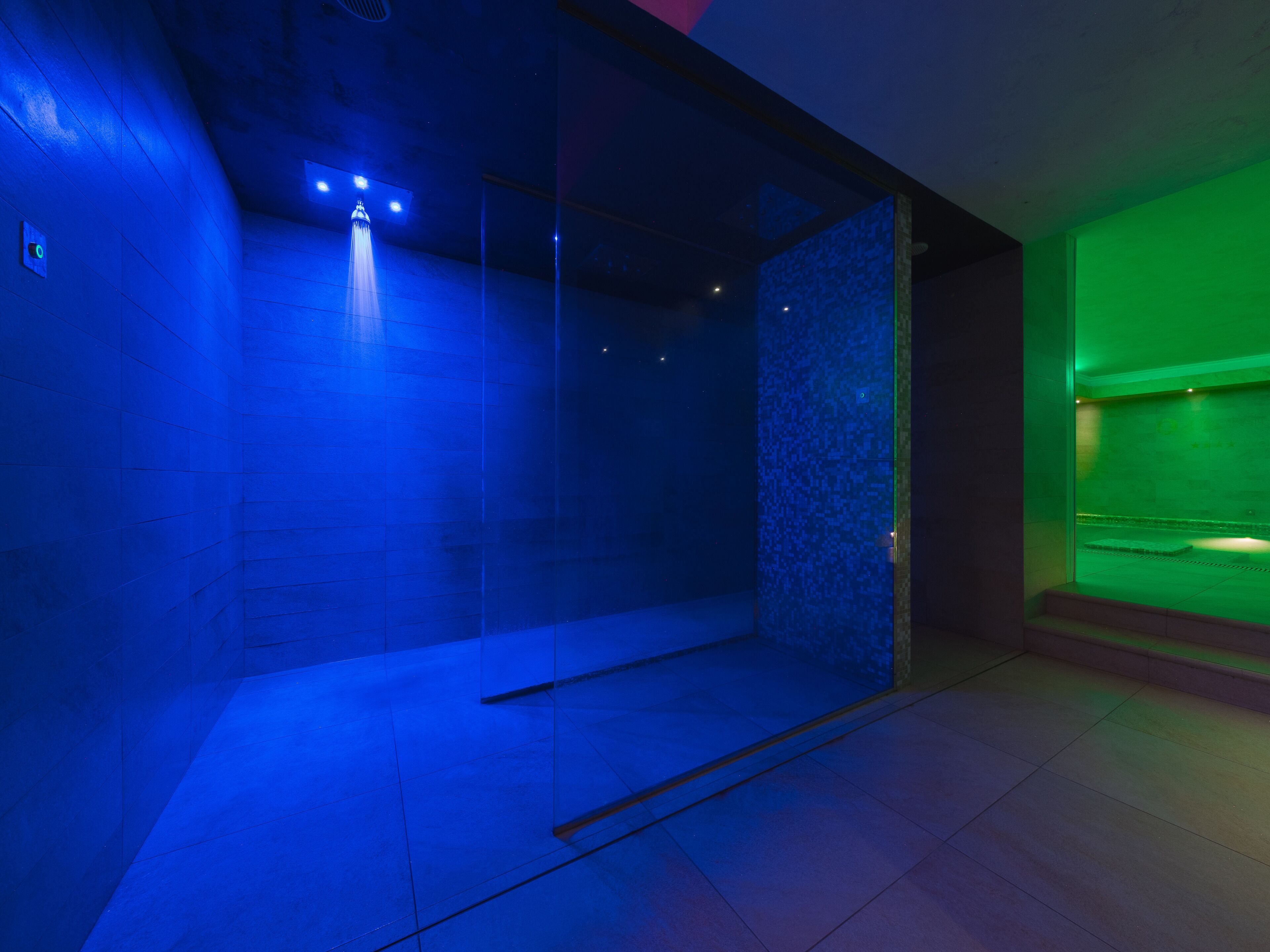 A modern spa room with a glass partition, a water feature, and a green-lit area.