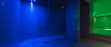 A modern spa room with a glass partition, a water feature, and a green-lit area.