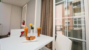 Ein Essbereich mit einem weißen Tisch, zwei Orangensaftgläsern, einem Teller mit einem Croissant und einer Vase mit Blumen.