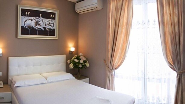Ein Hotelzimmer mit einem großen Bett, einem Nachttisch, einer Vase mit Blumen und einem Gemälde an der Wand.