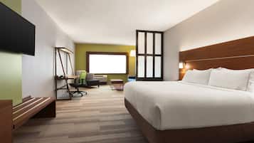 A hotel room with a large bed, a desk with a chair, a television, and a window with blinds.