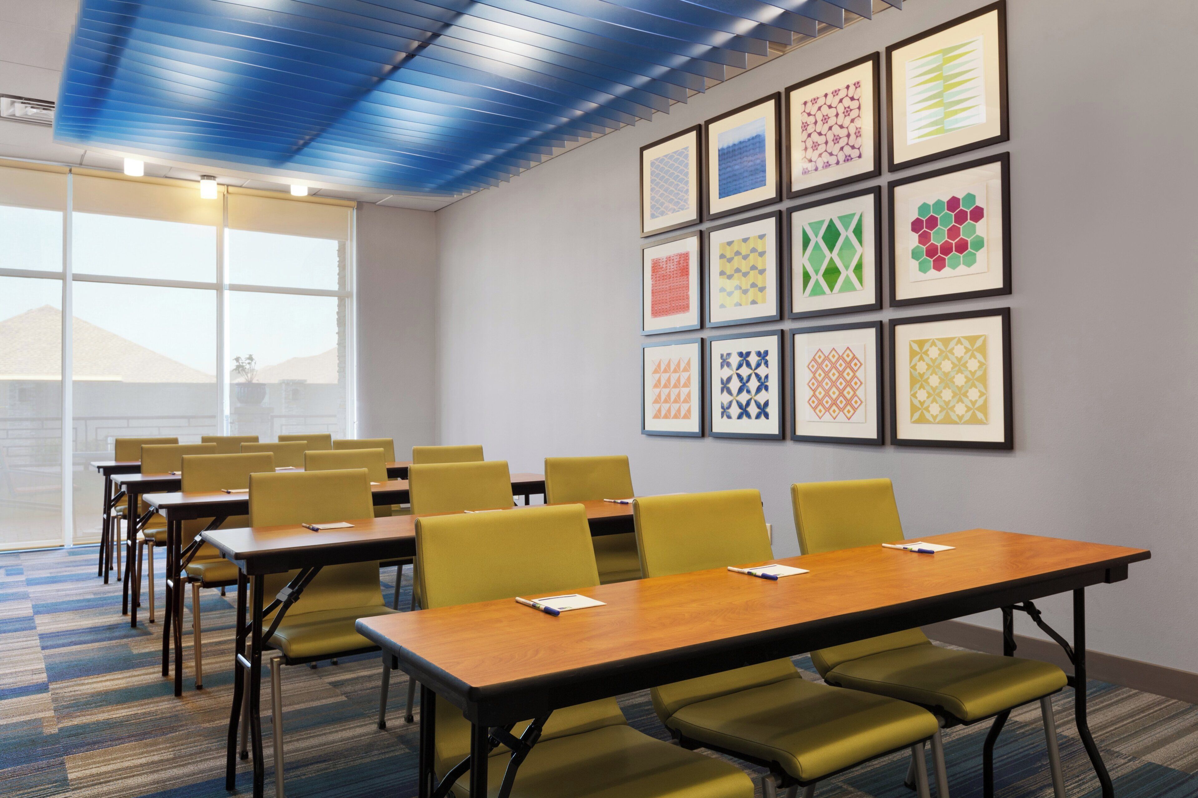 A conference room with tables and chairs, a large window, and a wall with framed geometric patterns.