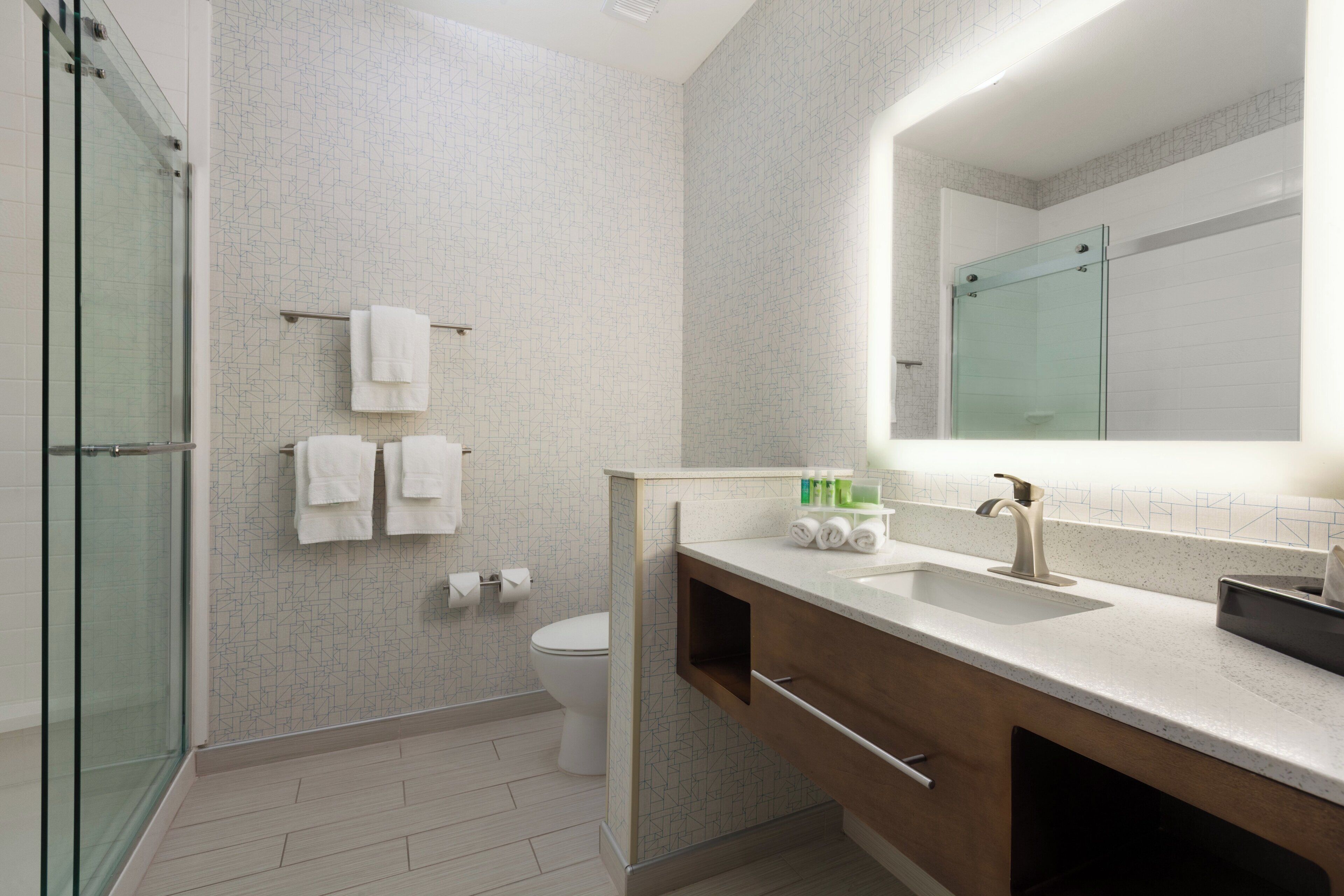 Un baño moderno con cabina de ducha de vidrio, inodoro y tocador con lavamanos y espejo.