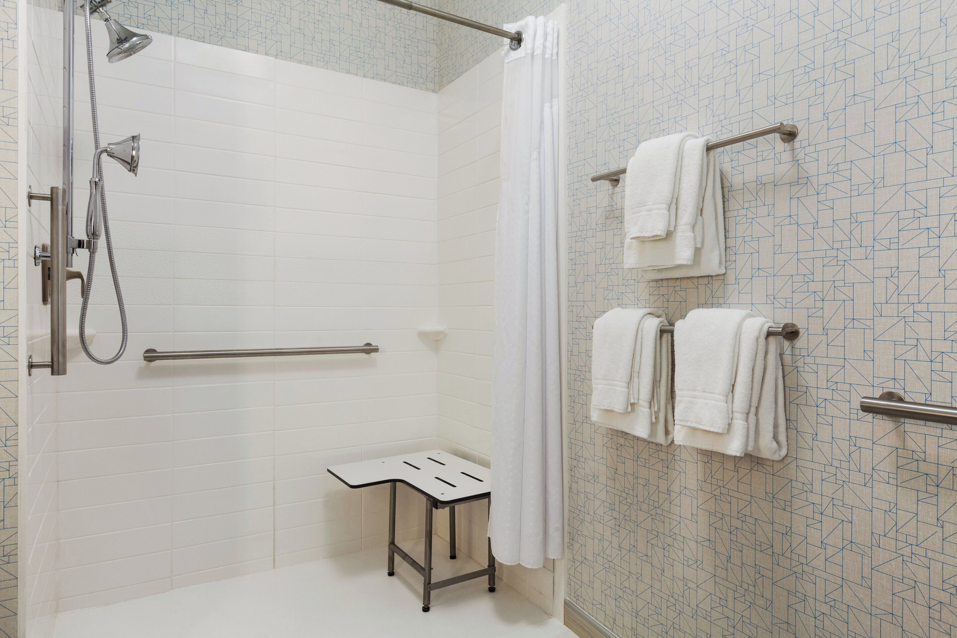 A shower area with a handheld showerhead, a glass-enclosed shower, a white towel rack, and a small step stool.