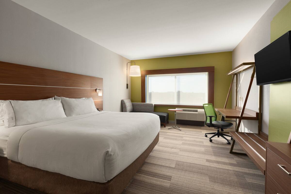 A hotel room with a large bed, a desk, a chair, a television, and a window with a view.