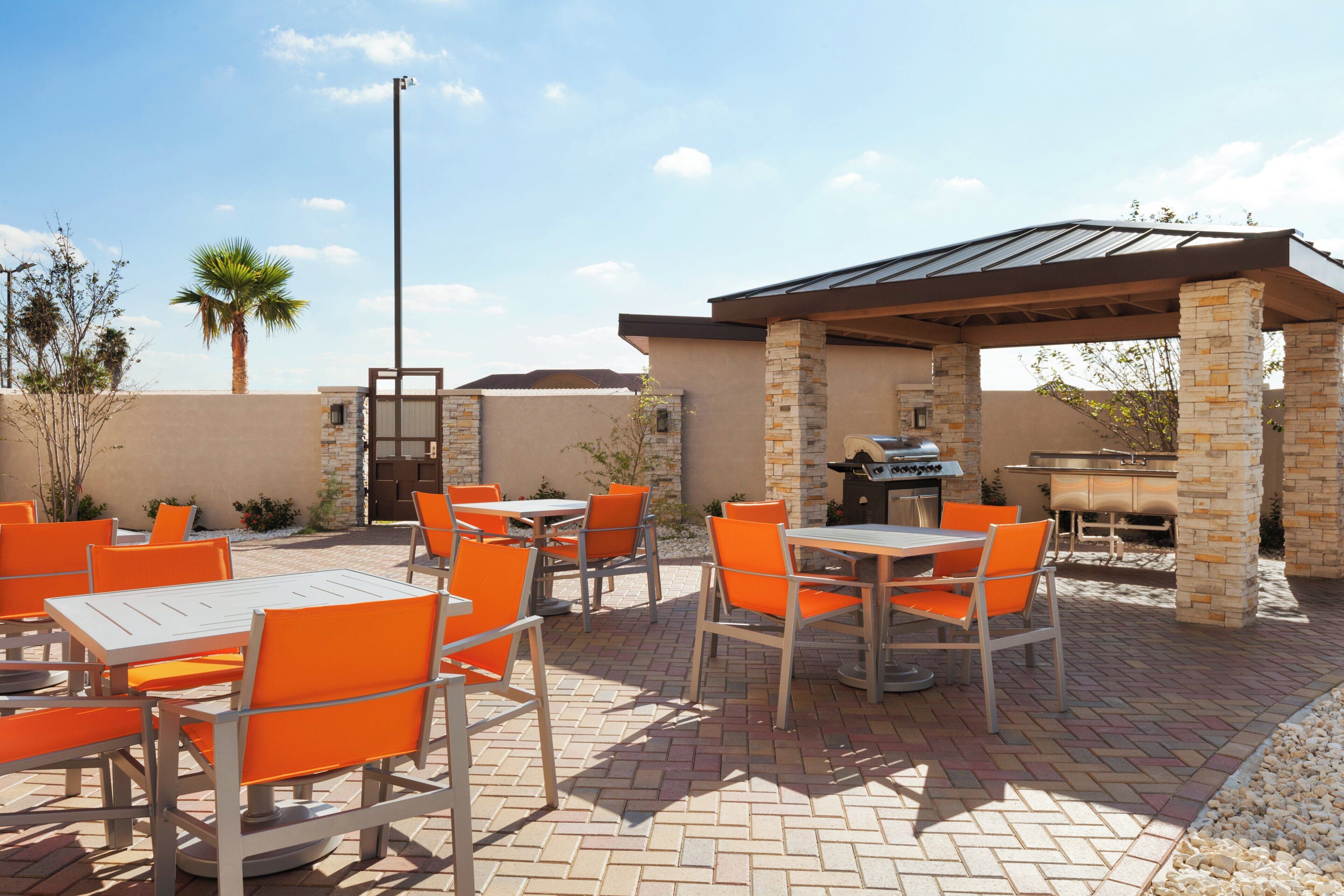 An outdoor patio with tables and chairs, a barbecue grill, and a pergola structure.