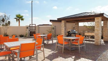 An outdoor patio with tables and chairs, a barbecue grill, and a pergola structure.