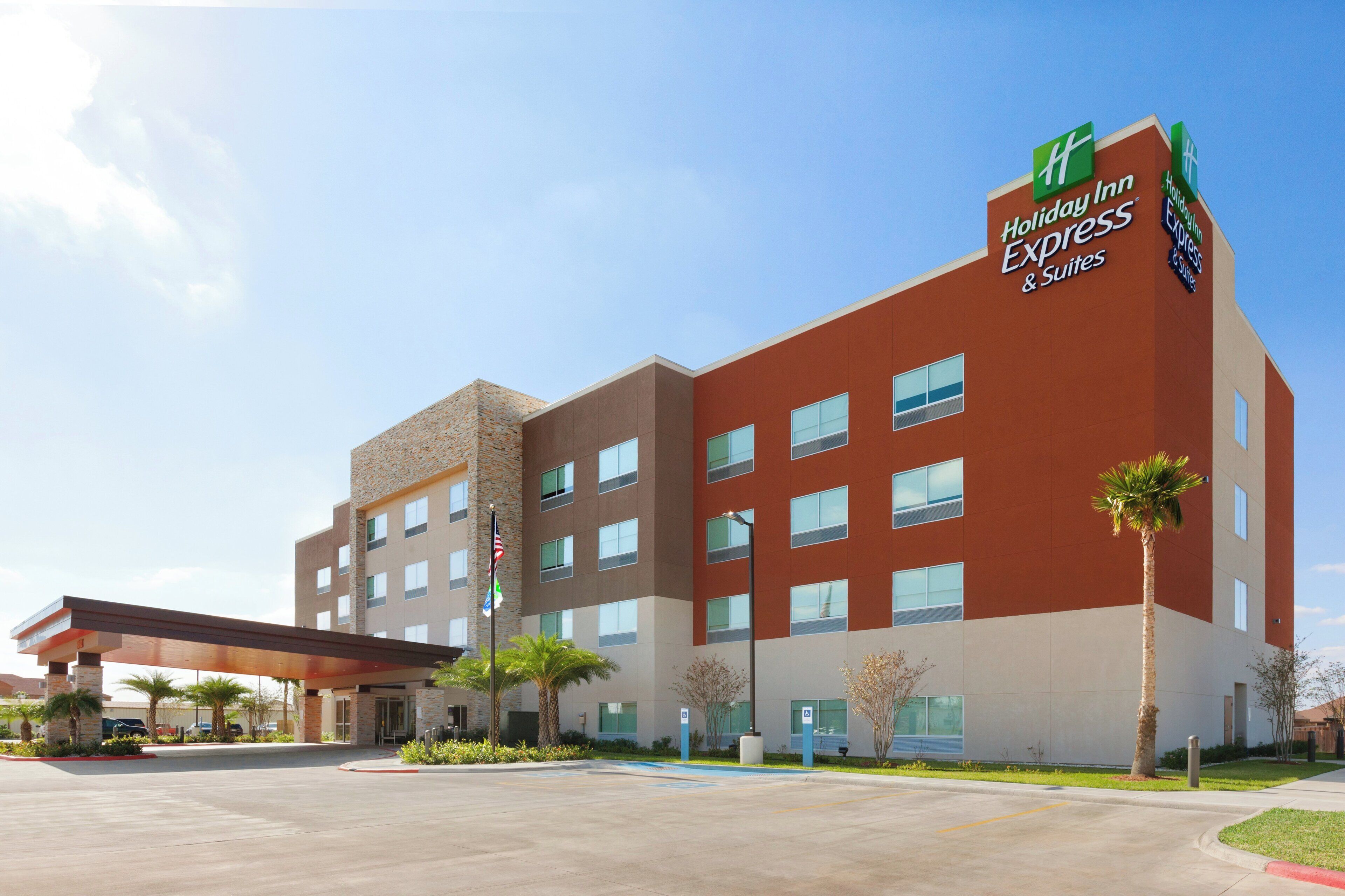 Un hotel Holiday Inn Express & Suites con un diseño moderno, que presenta techo plano, múltiples ventanales y cielo despejado.