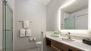 Un baño moderno con cabina de ducha de vidrio, inodoro y tocador con lavamanos y espejo.