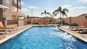 A swimming pool with lounge chairs and palm trees, surrounded by a building with stone and brick walls.