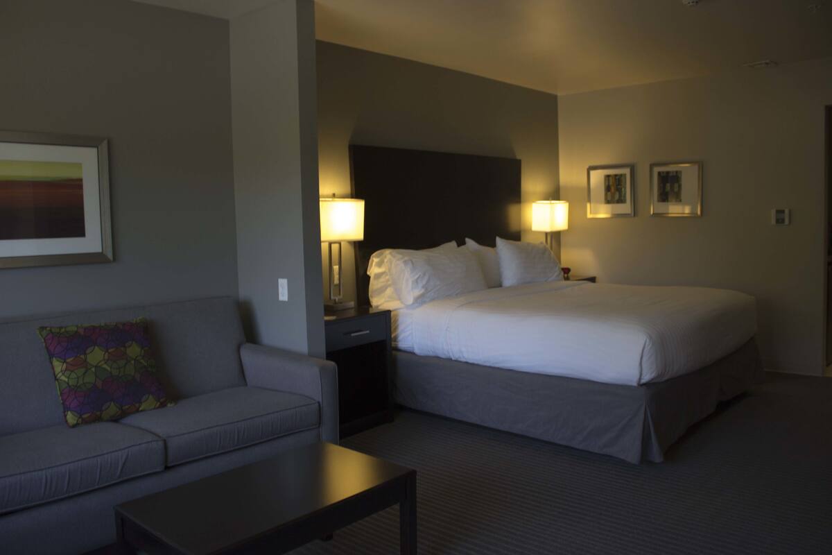 A hotel room with a bed, a sofa, a nightstand, and two wall-mounted lamps.