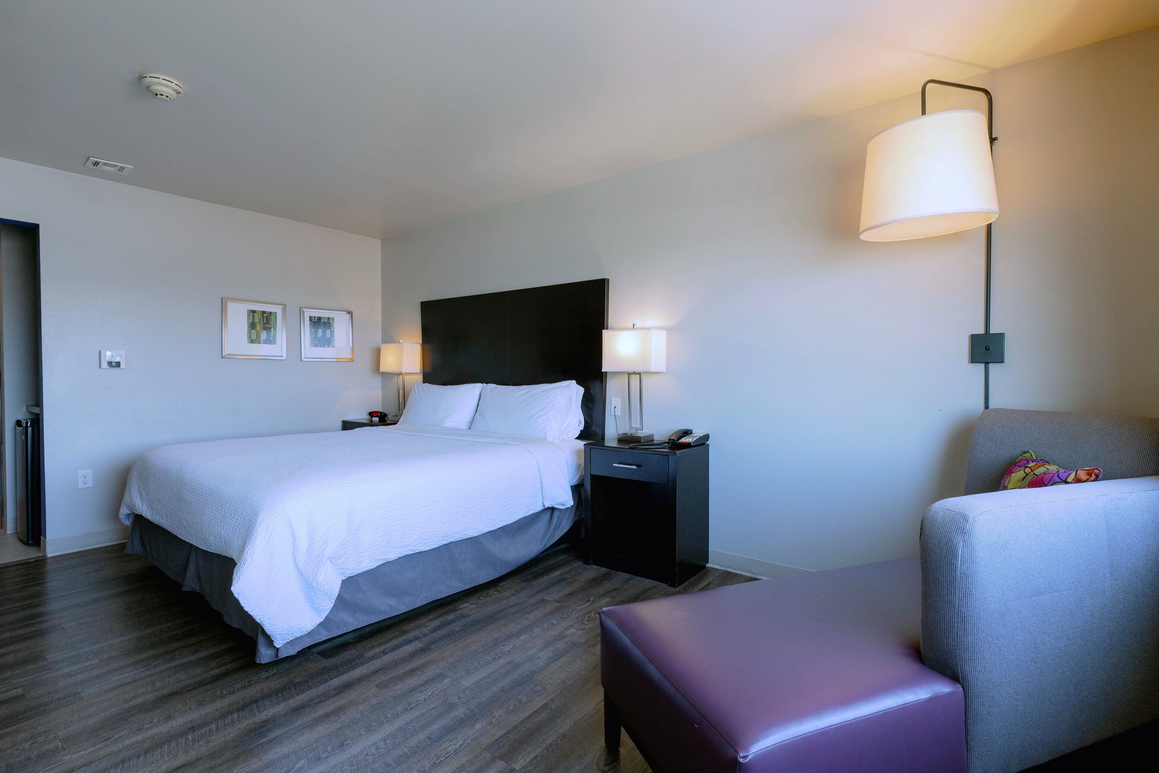 Una habitación de hotel con cama, mesitas de noche, una silla y una lámpara.