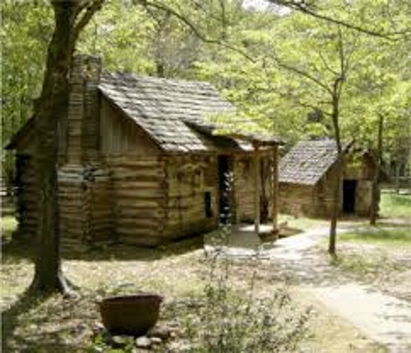 A rustic log cabin with a porch and a smaller structure nearby, surrounded by trees and greenery. - Holiday Inn Express & Suites Tahlequah by IHG (Tahlequah)