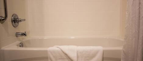 A white bathtub with a towel, chrome fixtures, and a shower head.