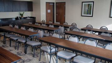 A conference room with multiple tables and chairs, a kitchenette, and an exit door.