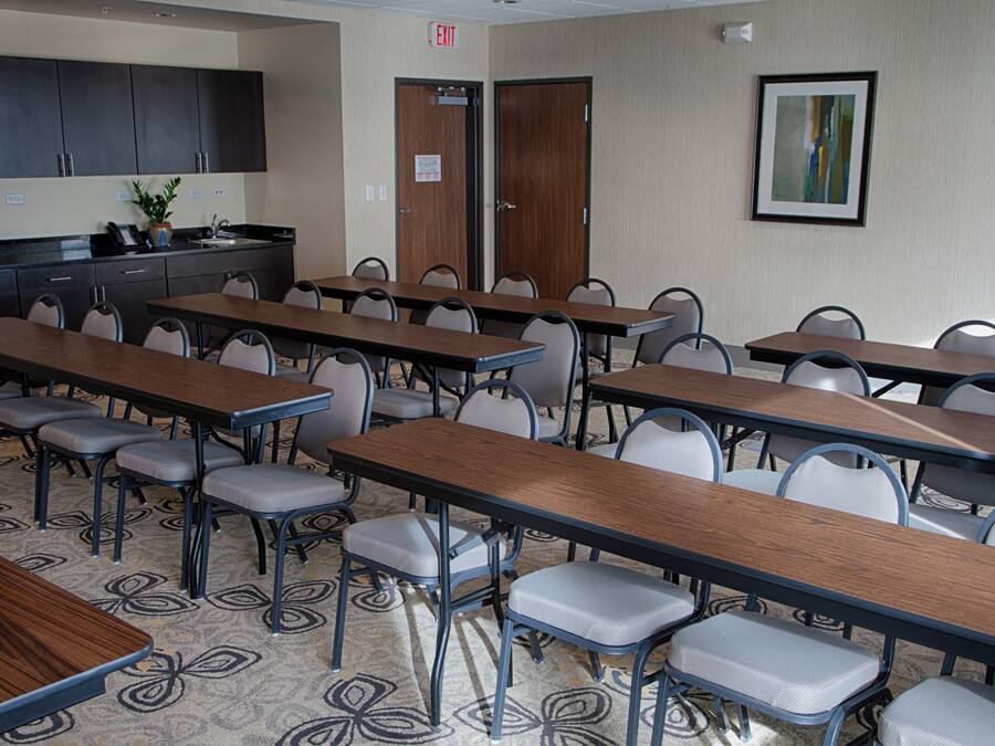 A conference room with multiple tables and chairs, a kitchenette, and an exit door.
