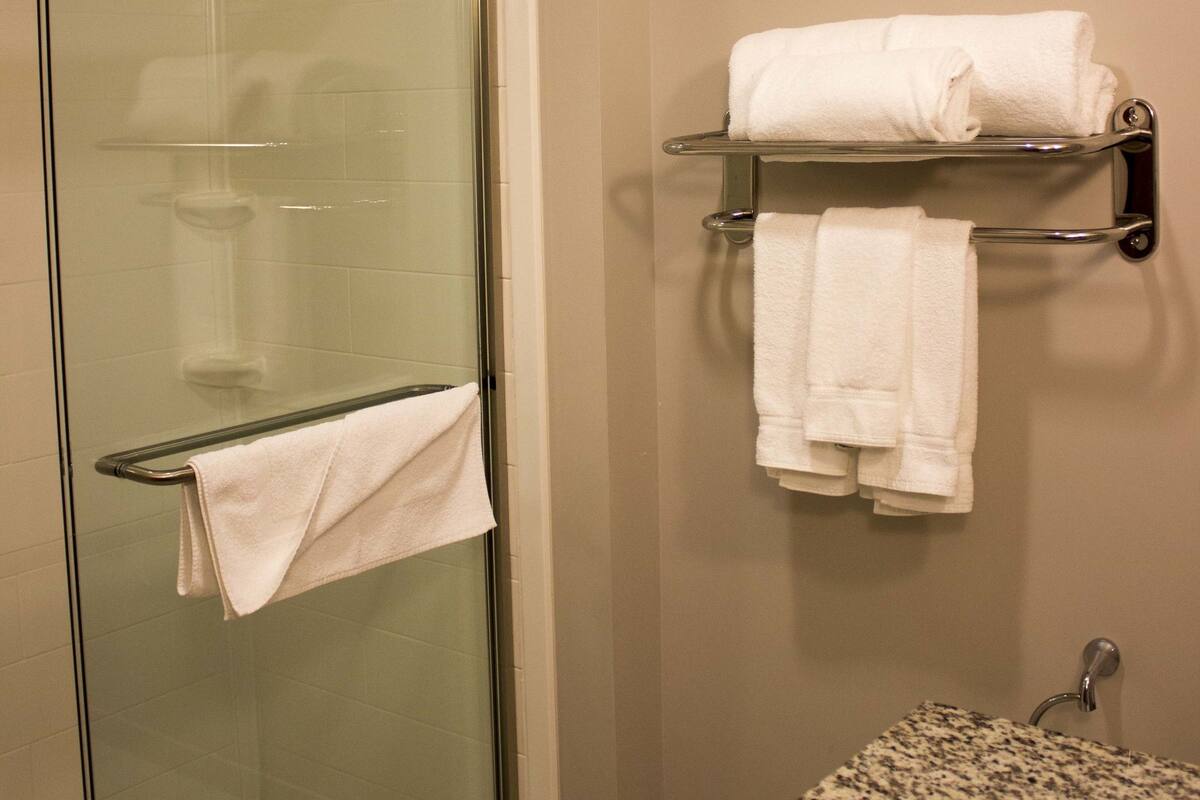 A bathroom with a glass-enclosed shower, a granite countertop sink, and a towel rack with folded towels.