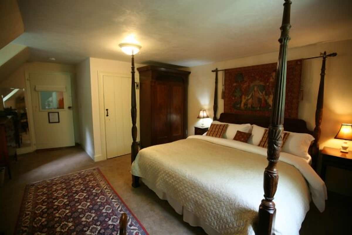 A four-poster bed with a canopy, a patterned rug, a nightstand with a lamp, and a painting on the wall.