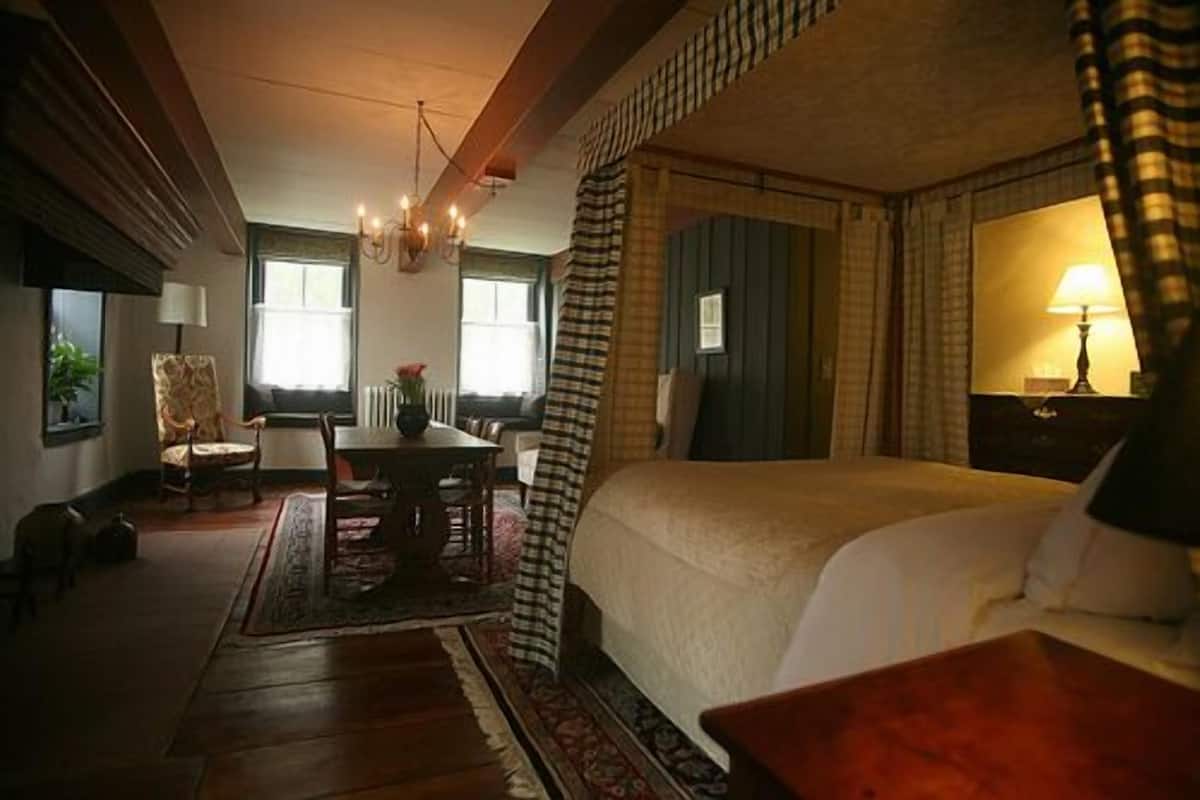 A bedroom with a large bed, a desk, and a chair. There is a window with a view of the outside.