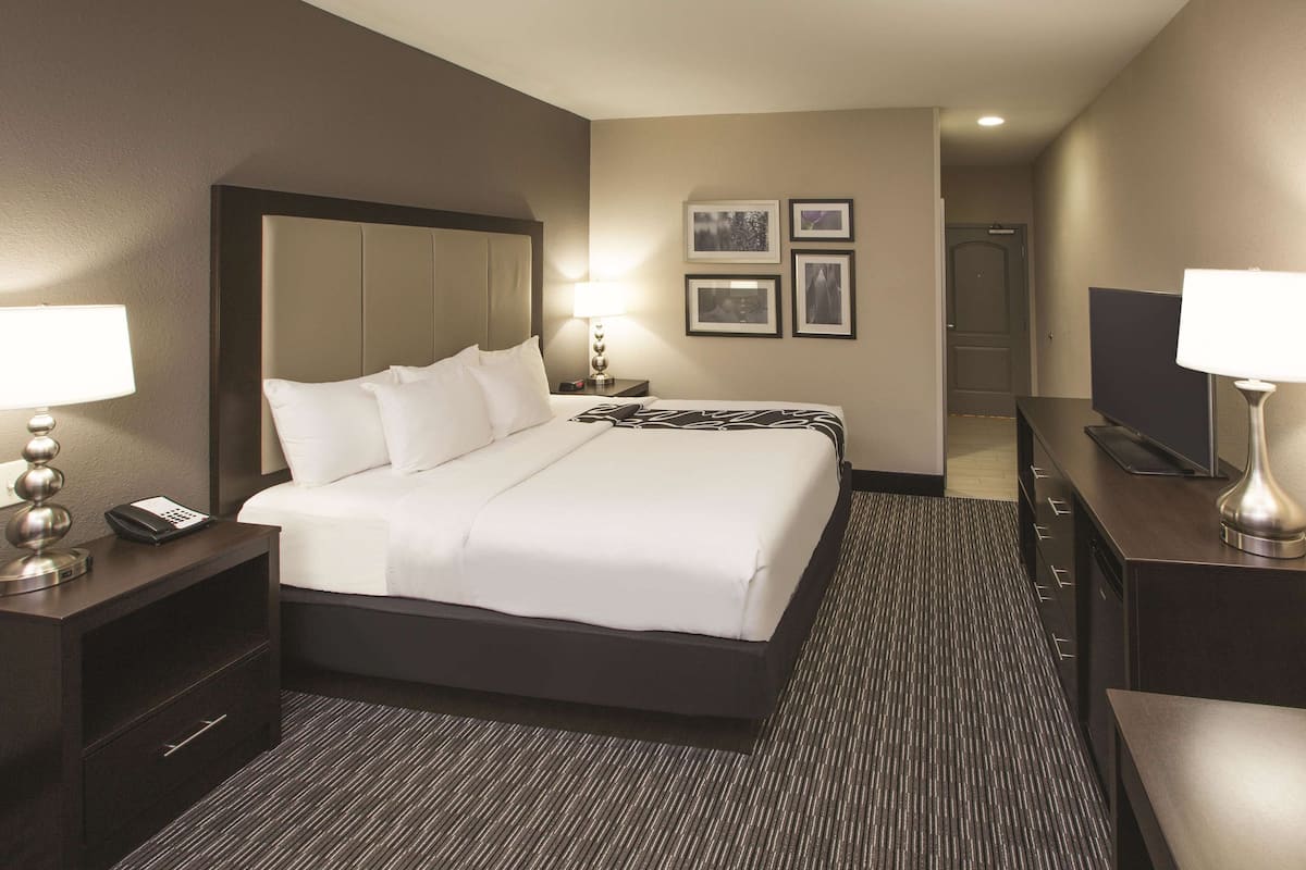 A hotel room with a large bed, bedside tables with lamps, a flat-screen TV, and framed pictures on the wall.