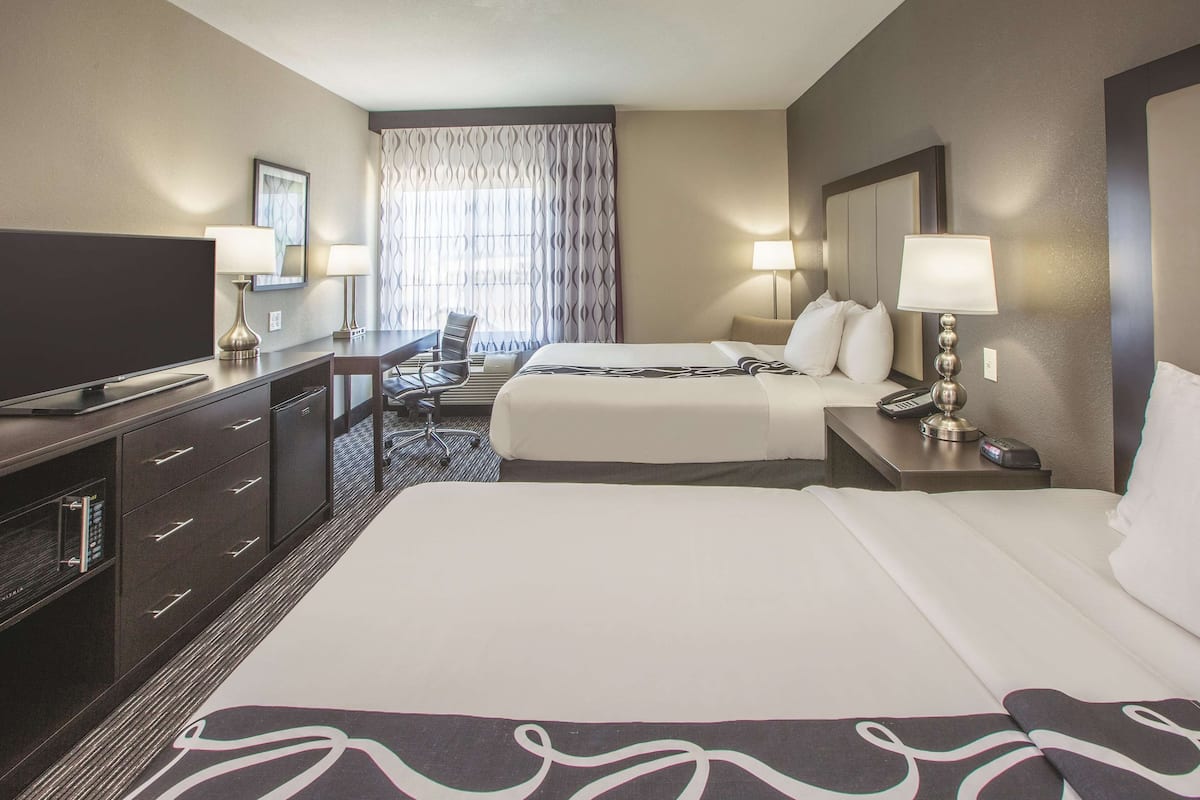 A hotel room with two beds, a desk, a chair, a TV, and a window with curtains.