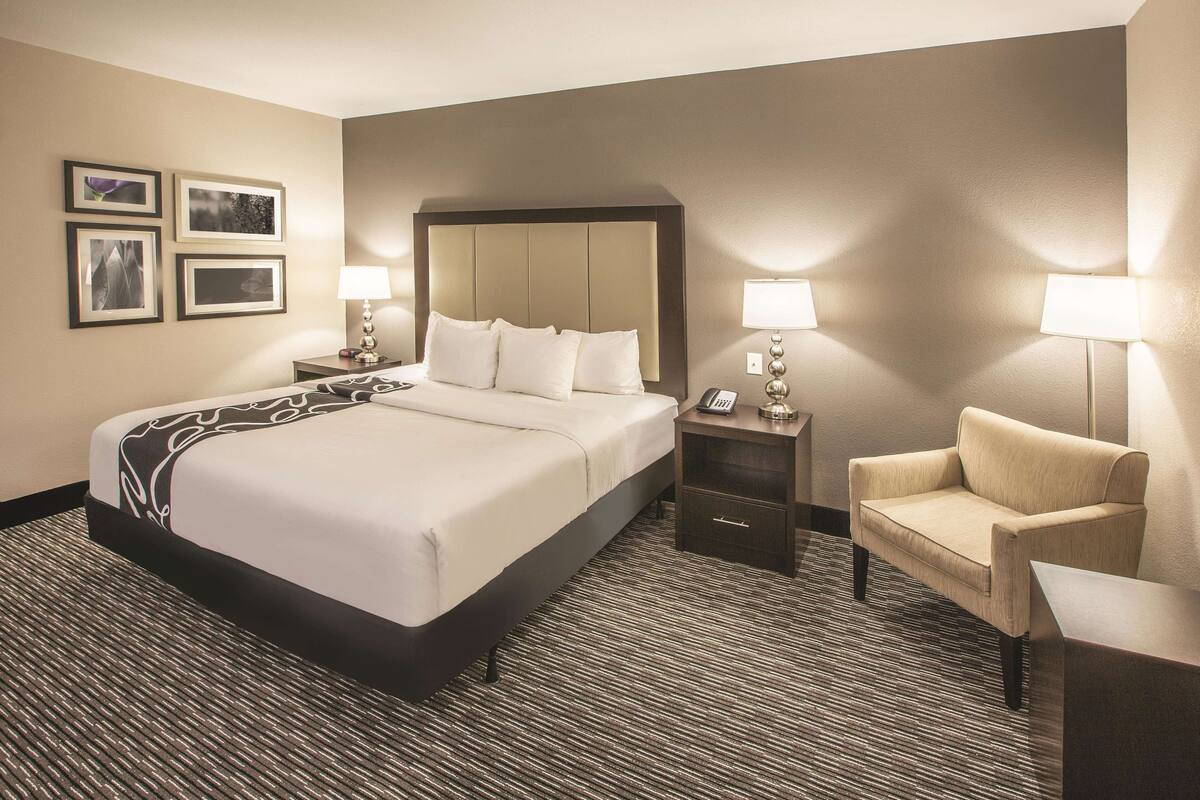 A hotel room with a large bed, two bedside tables, a chair, and a carpeted floor.