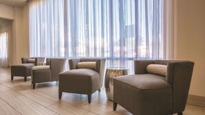 Una sala de estar moderna con cuatro sillones, una mesita auxiliar, ventanas amplias con cortinas translúcidas y suelo de madera.