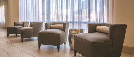 Una sala de estar moderna con cuatro sillones, una mesita auxiliar, ventanas amplias con cortinas translúcidas y suelo de madera.