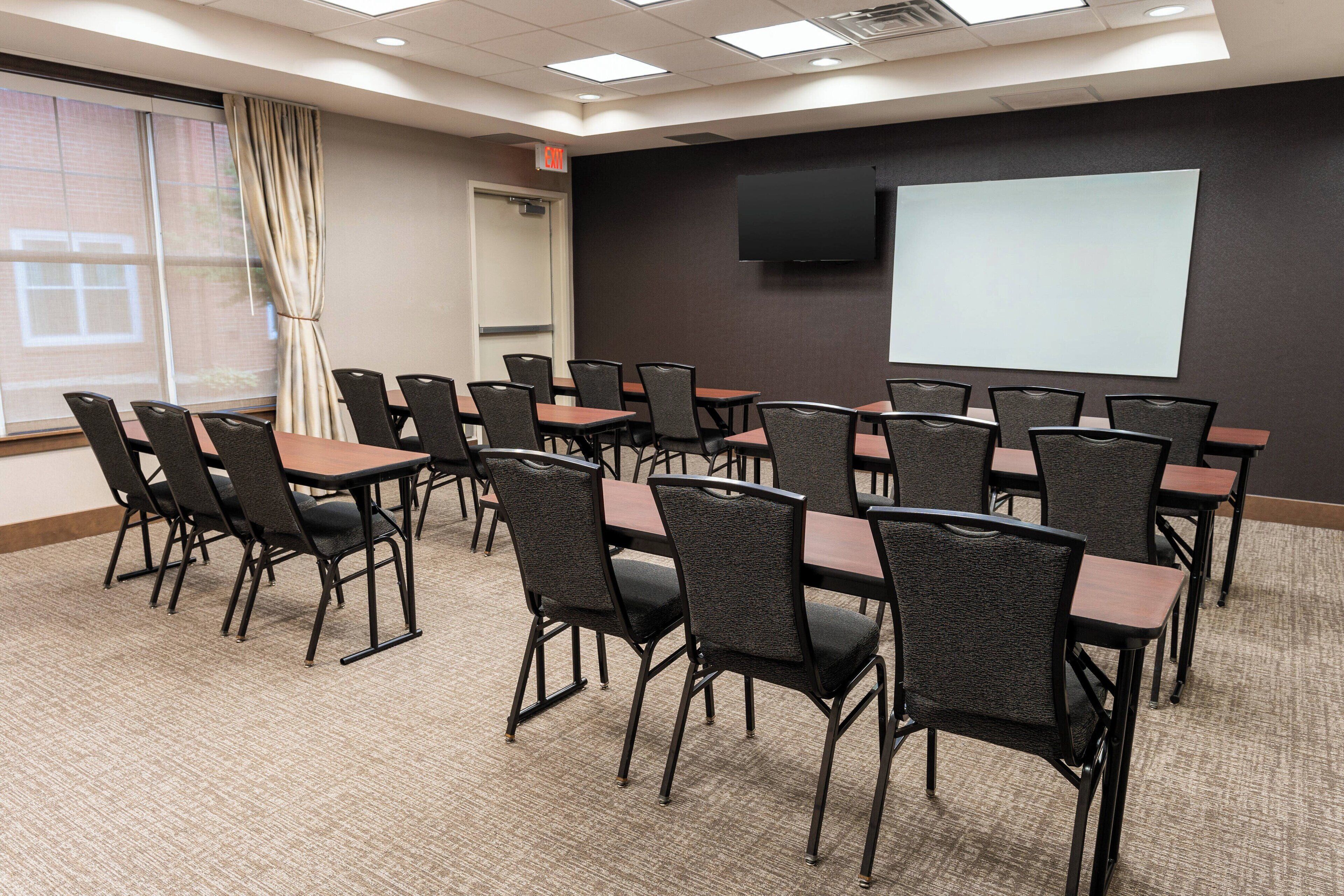 A conference room with multiple tables and chairs, a projector screen, and a large window with curtains.