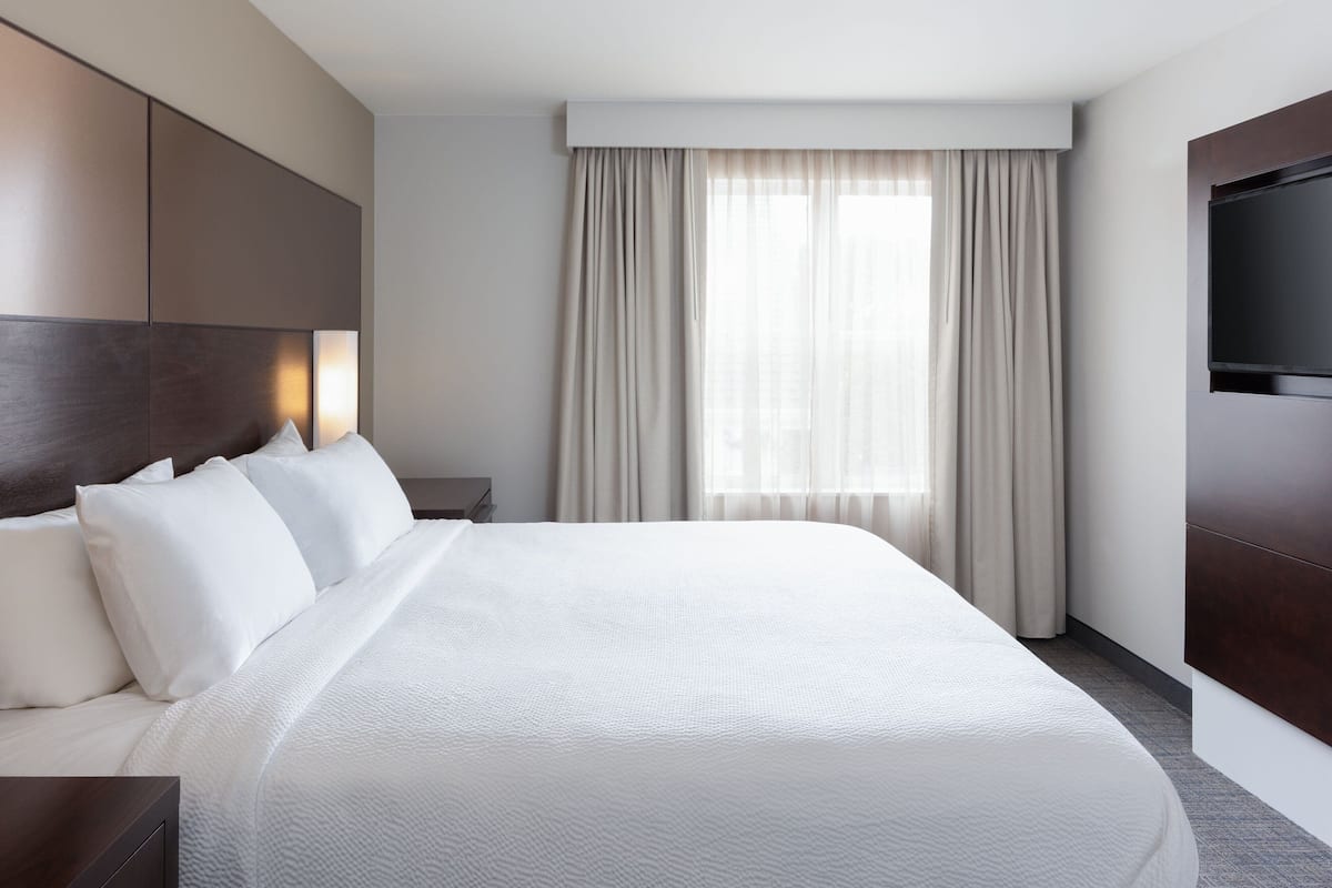 A hotel room with a large bed, a flat-screen TV mounted on the wall, and a window with curtains.
