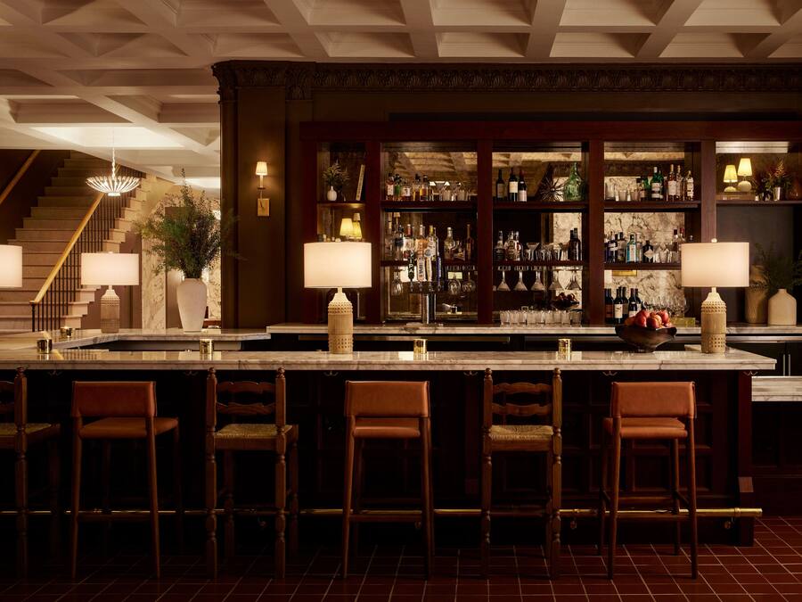 A bar area with a marble countertop, multiple bar stools, and a variety of bottles and glasses.