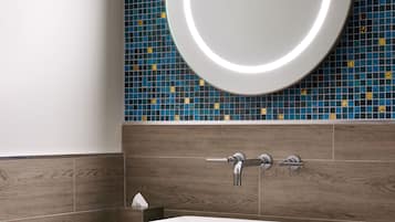 Un baño con un lavamanos blanco, un espejo redondo con luz y una pared de azulejos de mosaico azul.