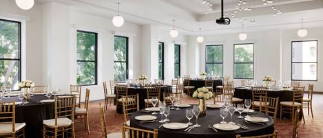 Un amplio salón de banquetes con mesas redondas dispuestas para comer, ventanas grandes y modernas lámparas.