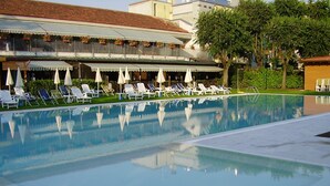 A swimming pool with lounge chairs and umbrellas, surrounded by a building with a balcony. - Hotel Sporting Brugherio (Brugherio)