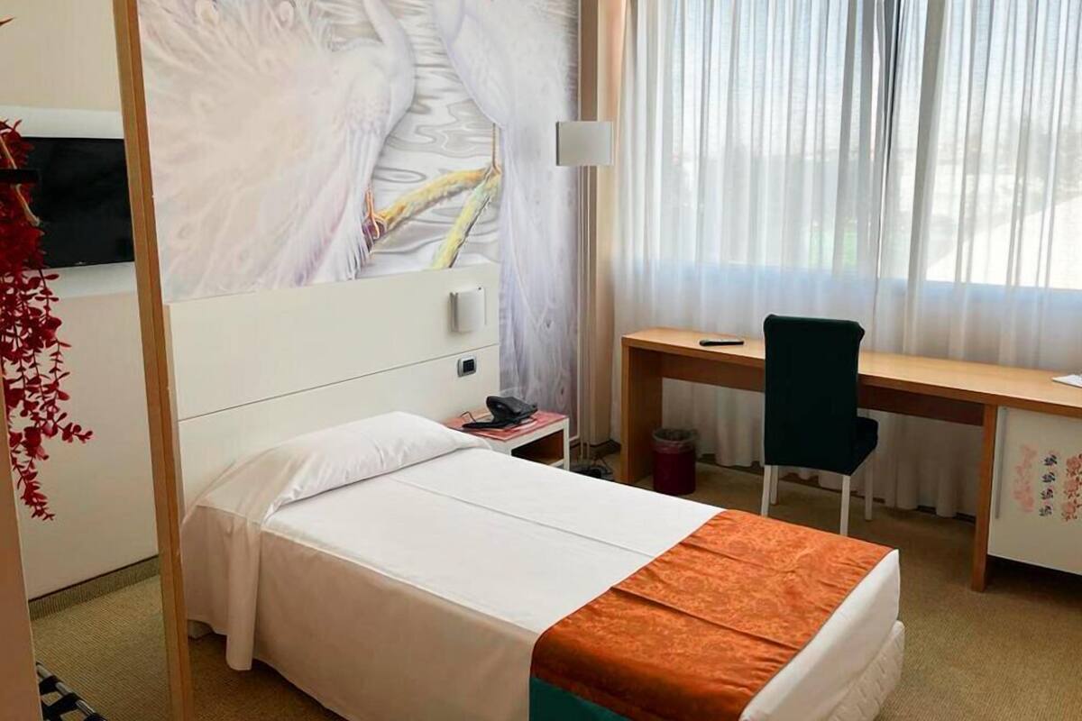 Une chambre d’hôtel équipée d’un lit, d’un bureau, d’une chaise, d’une télévision et d’une fenêtre avec des rideaux.