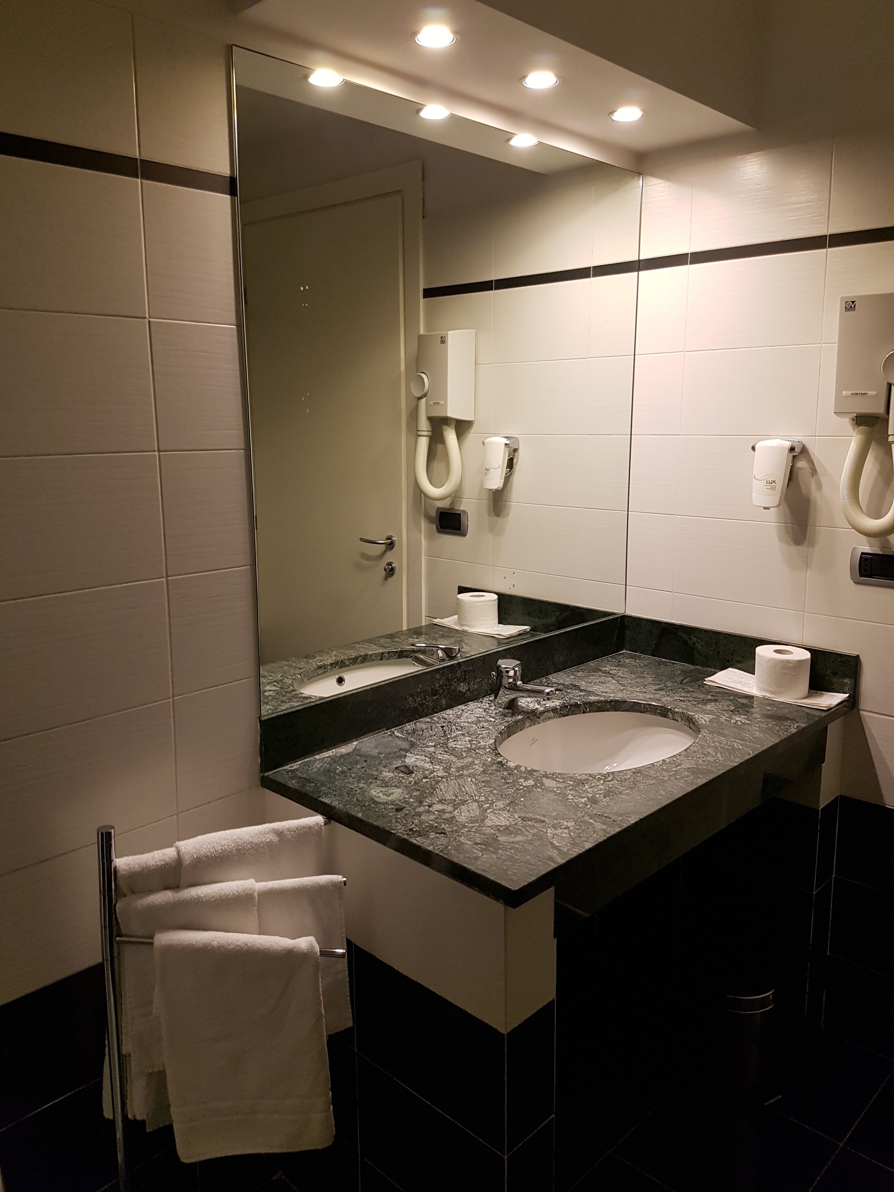 Un baño moderno con un espejo grande, lavamanos dobles y un perchero para toallas.