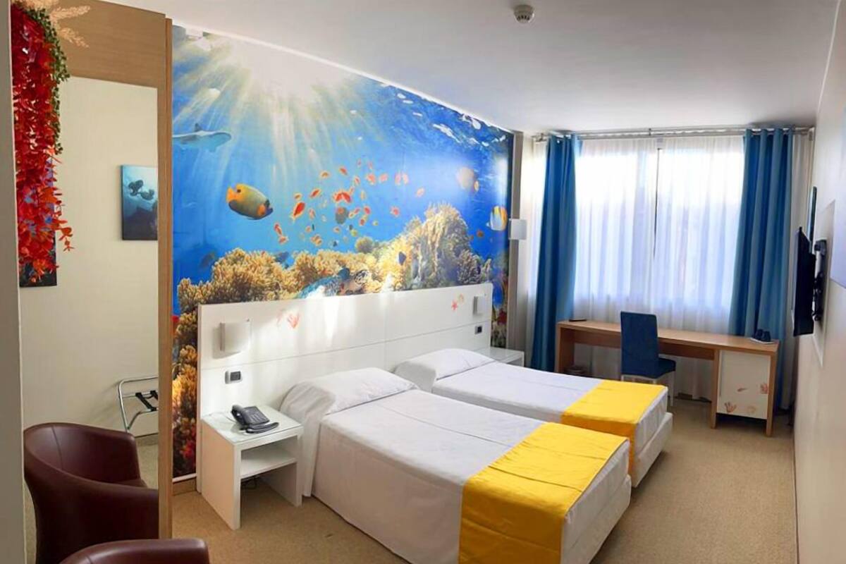 Une chambre d’hôtel avec deux lits, un bureau, une chaise et une grande fresque murale représentant une scène sous-marine.