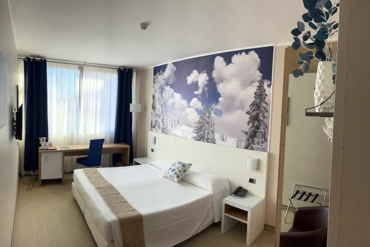 Une chambre d’hôtel équipée d’un lit, d’un bureau, d’une chaise, d’une table de chevet et d’un téléphone fixé au mur.
