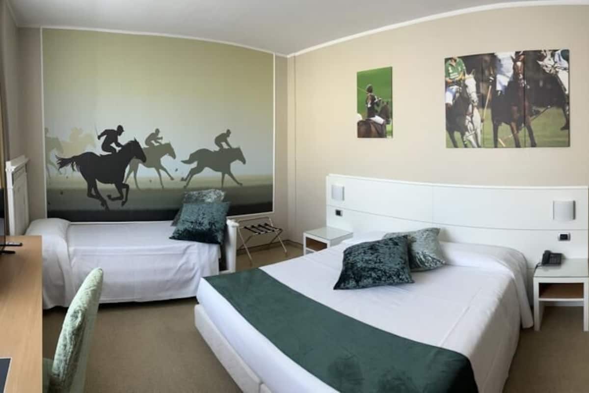 Une chambre d’hôtel avec deux lits, un bureau et une chaise. Les murs sont décorés d’œuvres d’art représentant des chevaux et des cavaliers.