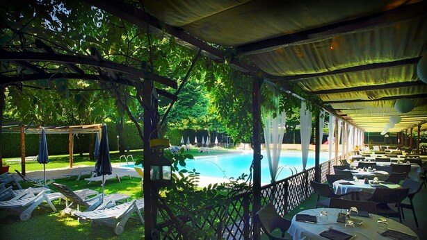 A covered outdoor area with a pool, lounge chairs, and tables set up for dining. - Hotel Sporting Brugherio (Brugherio)
