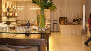 A hotel dining area with a glass table set for a meal, a vase with flowers, and a bar with bottles and glasses in the background. - Hotel Sporting Brugherio (Brugherio)
