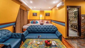A hotel room with a blue sofa, a bed with a headboard, a small table with fruit and a vase, and a bathroom visible through a mirror. - Hotel Yukhang (Kathmandu)