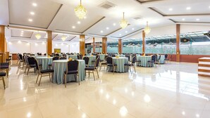 A spacious banquet hall with round tables and chairs, chandeliers, and large windows. - Hotel Yukhang (Kathmandu)