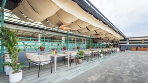 An outdoor seating area with tables and chairs, potted plants, and a covered section with a striped awning. - Hotel Yukhang (Kathmandu)