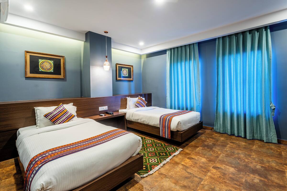 A hotel room with two beds, a nightstand, a lamp, and a window with curtains.